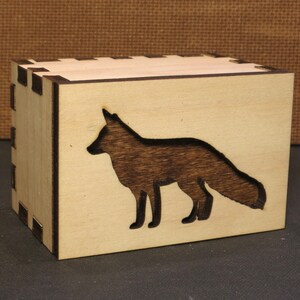 May include: A wooden box with a fox silhouette cutout. The box is made of light wood with a natural finish. The fox is dark brown and is facing to the right.