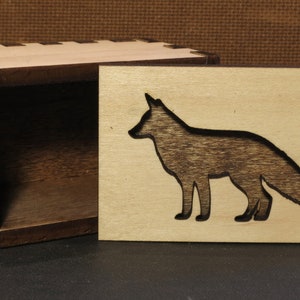 May include: A wooden box with a fox silhouette cutout on the lid. The box is made of light wood with a dark wood interior.
