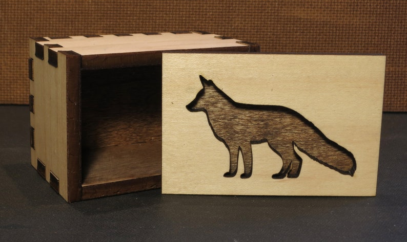May include: A wooden box with a fox silhouette cutout on the lid. The box is made of light wood with a dark wood interior.