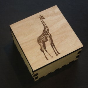 May include: A wooden box with a laser-engraved image of a giraffe. The box is light brown and has a dark brown border.