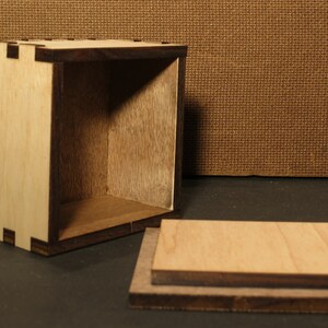 May include: A wooden box with a lid, the box is made of light wood with a dark wood trim. The box is open and the lid is laying next to it.