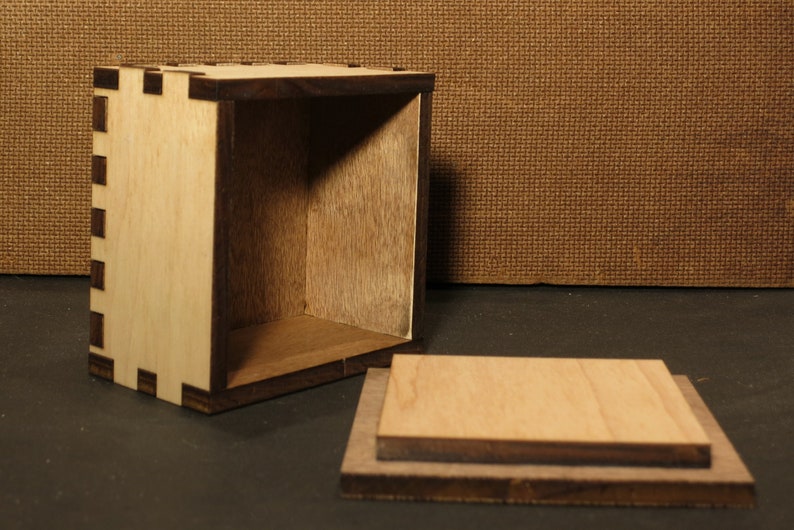 May include: A wooden box with a lid, the box is made of light wood with a dark wood trim. The box is open and the lid is laying next to it.