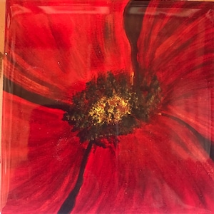 Puede incluir: Pintura cuadrada de una flor de amapola roja. Los pétalos rojos vibrantes irradian desde un centro oscuro con acentos amarillos. La obra de arte está encerrada en un acabado transparente y brillante.