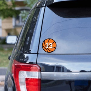 May include: A black car with a basketball decal on the back window. The basketball is orange and has the number 13 on it.