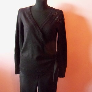 Puede incluir: Suéter negro de punto con un adorno de cuentas en el hombro. El suéter tiene manga larga y un lazo en la cintura.