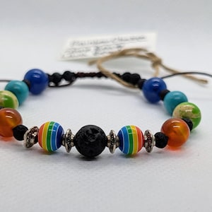 May include: A colorful beaded bracelet featuring a variety of beads in shades of blue, green, orange, and rainbow. The bracelet includes a black lava bead and is strung on a black cord. A small silver leaf charm hangs from the cord.