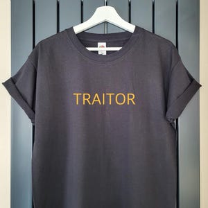 May include: A black t-shirt with the word "TRAITOR" printed in yellow on the front.