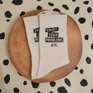 May include: A pair of white socks with black text that reads "Enjoy your problems Bye."