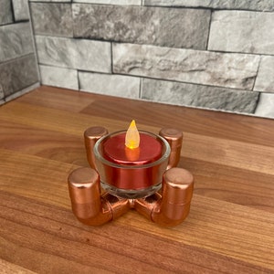 May include: A copper candle holder with a red tea light candle inside. The candle holder is made of copper pipe fittings and has a rustic look.