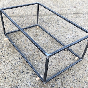 May include: A black metal frame with wooden blocks at the base. The frame is rectangular and appears to be a base for a table or other furniture.
