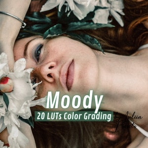 Op de afbeelding: Een vrouw met blauwe ogen en roze lippen ligt op een bed van witte bloemen. De tekst "Moody 20 LUTs Color Grading by Julia Presets" is over de afbeelding gelegd.