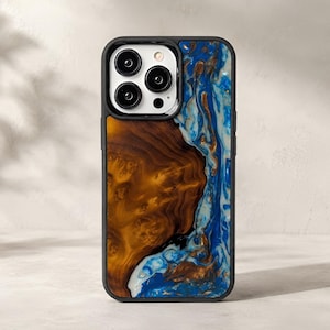 May include: A smartphone case featuring a split design with a dark brown wood grain section on the left and a swirling blue, white, and gold resin pattern on the right. The case has a black frame and a cutout for a triple-lens camera system.