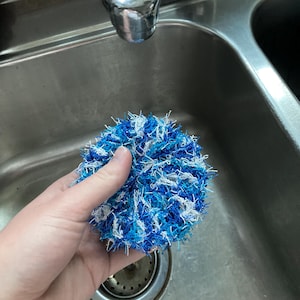 May include: A blue and white crocheted dish scrubby in a stainless steel kitchen sink.