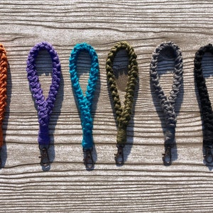 May include: Seven colorful braided keychains with metal clasps. The keychains are orange, purple, blue, green, gray, and black.