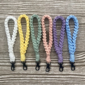 May include: Six crocheted lanyards in different colors, including white, yellow, green, pink, purple, and blue. Each lanyard has a metal clasp at the end.