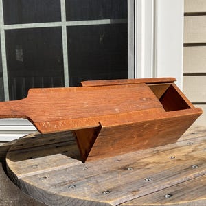 May include: A wooden box with a hinged lid and a handle. The box is made of unfinished wood and has a rustic appearance.