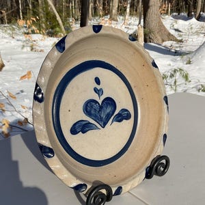 May include: A blue and white ceramic pie plate with a heart design. The plate is on a black metal stand.