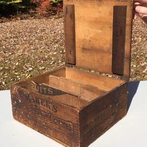 May include: A vintage wooden box with a hinged lid. The box is labelled "Baker's Chocolate Factory" and has a compartment for storing nuts.