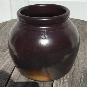 May include: A dark brown glazed ceramic crock with a metal handle. The crock has a number "3" stamped on the side.
