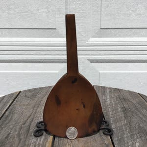 May include: A vintage wooden scoop with a long handle and a wide, rounded bowl. The scoop is a warm brown colour and appears to be handmade. A coin is placed next to the scoop for size reference. The scoop is on a wooden table.
