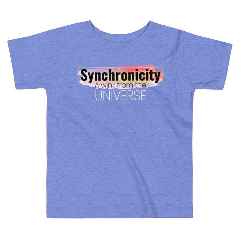 Op de afbeelding: Een lichtblauw T-shirt voor peuters met een kleurrijk abstract ontwerp en de tekst "Synchronicity A wink from the UNIVERSE" in zwart.
