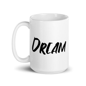 May include: White ceramic coffee mug with a black handwritten word "DREAM" on the front.