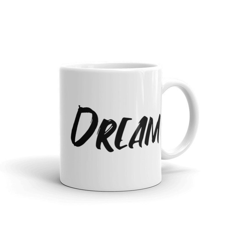 May include: White ceramic coffee mug with a black handwritten inscription that reads "DREAM BIG".