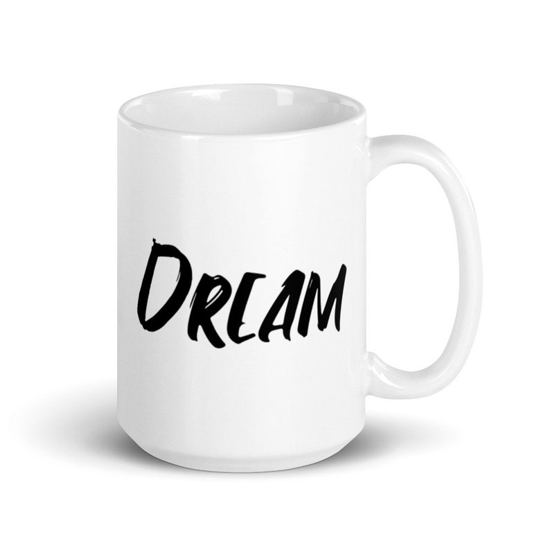 May include: White ceramic coffee mug with a black handwritten word "DREAM" on the front.