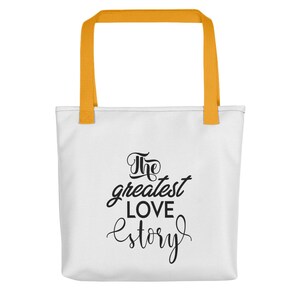 K&ouml;nnte beinhalten: Wei&szlig;e Einkaufstasche mit gelben Henkeln. Die Tasche hat schwarzen Text mit der Aufschrift "The greatest love story."
