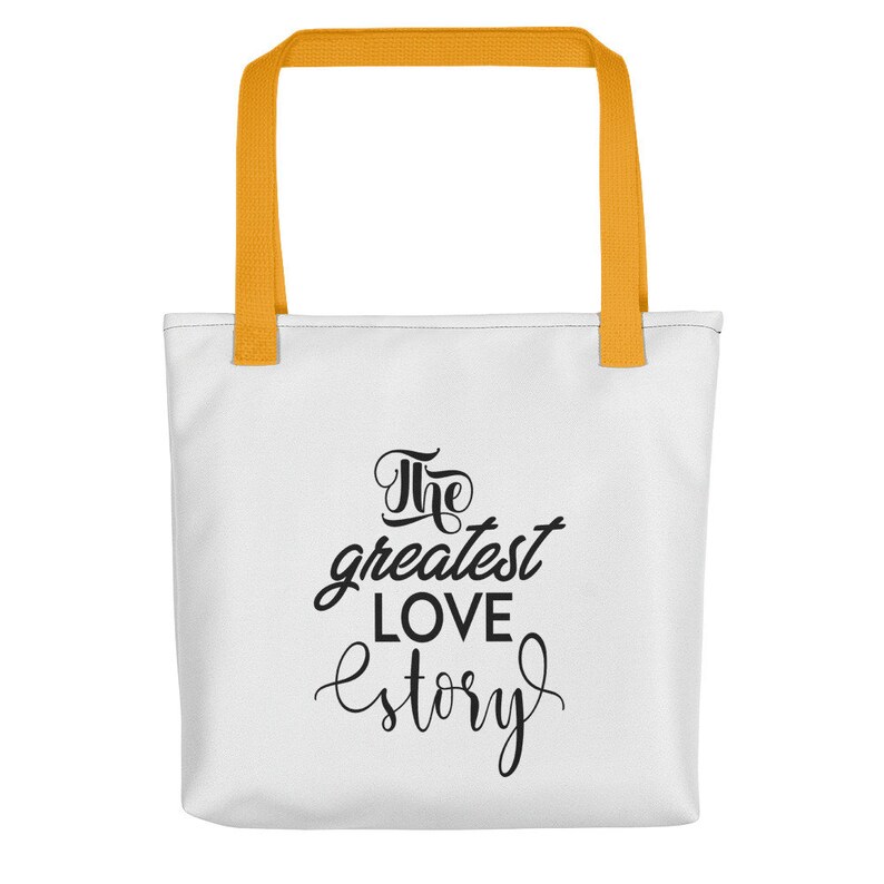 K&ouml;nnte beinhalten: Wei&szlig;e Einkaufstasche mit gelben Henkeln. Die Tasche hat schwarzen Text mit der Aufschrift "The greatest love story."