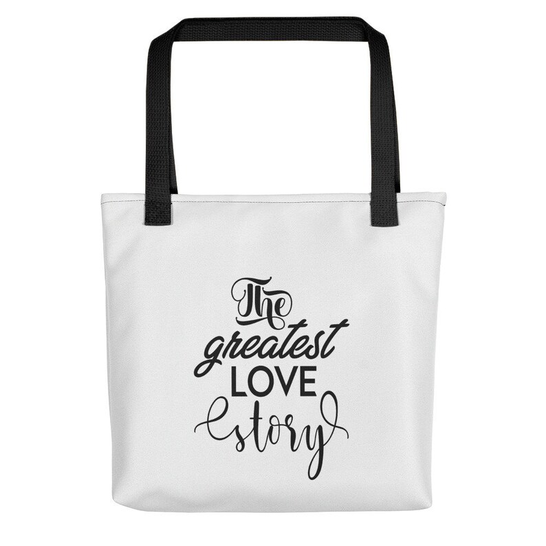 K&ouml;nnte beinhalten: Wei&szlig;e Einkaufstasche mit schwarzen Henkeln und dem Text "The greatest love story" in schwarzer Schrift.
