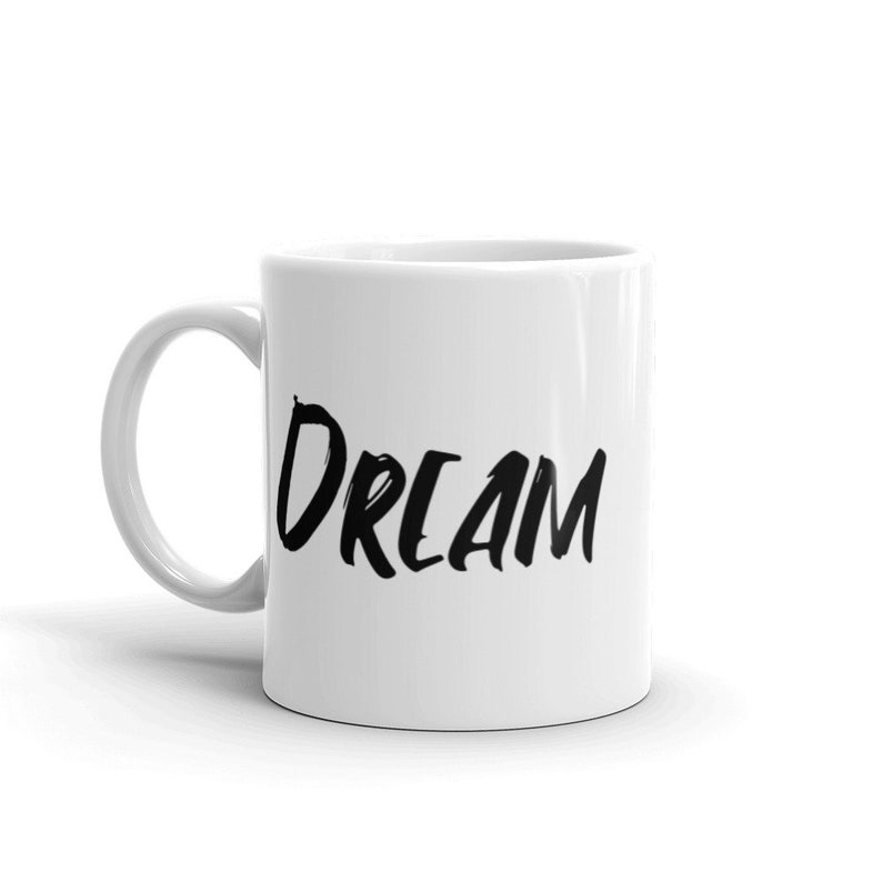 May include: White ceramic coffee mug with a black handwritten word "DREAM" on the side.