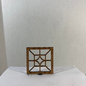 Puede incluir: Un panel de ventana de madera con un diseño geométrico. El panel de ventana está hecho de madera marrón claro y tiene una forma cuadrada.