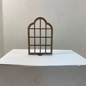 Peut inclure: Une découpe en bois d'une fenêtre cintrée avec plusieurs carreaux. La fenêtre est brune et a un design simple.