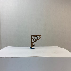 Puede incluir: Un soporte de estante decorativo de madera con un diseño tallado. El soporte es de color marrón y tiene un acabado de madera clara. Está sentado sobre una superficie blanca.