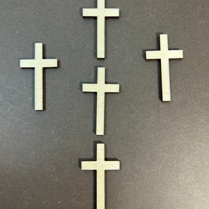 May include: Five wooden crosses arranged in a pyramid shape on a gray background. The crosses are all the same size and shape, and they are all made of light-colored wood.
