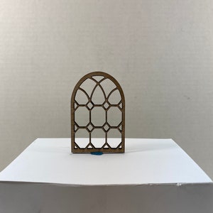 Peut inclure: Une découpe en bois d'une fenêtre en vitrail avec un motif géométrique. La fenêtre est cintrée en haut et a une finition en bois brun.