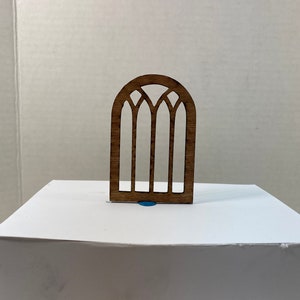 May include: A wooden cutout of a stained glass window with a pointed arch and four vertical panes. The window is brown and has a rustic look.