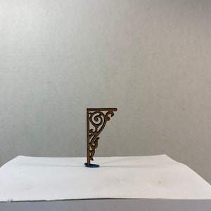 Puede incluir: Un soporte de esquina decorativo de madera con un diseño de desplazamiento detallado. El soporte es de color marrón claro y tiene un acabado de madera natural.