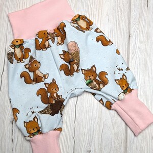 Könnte beinhalten: Babyhose mit hellblauem Muster von braunen Eichhörnchen, die Eiswaffeln und Eicheln halten. Die Bündchen und der Bund sind einfarbig rosa.