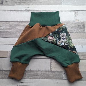 Könnte beinhalten: Grüne und braune Babyhose mit Waldtier-Druck. Die Hose hat eine weite Beinweite und einen umgeschlagenen Saum.
