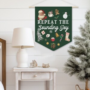 May include: A green Christmas banner with the text "Repeat the Sounding Joy" and various Christmas icons, including Santa Claus, a snowman, a gingerbread man, and a stocking. The banner is hanging on a white wall in a bedroom setting.