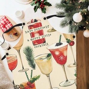 May include: White kitchen apron with a festive Christmas design featuring a variety of cocktails and the text "have yourself a merry little cocktail".