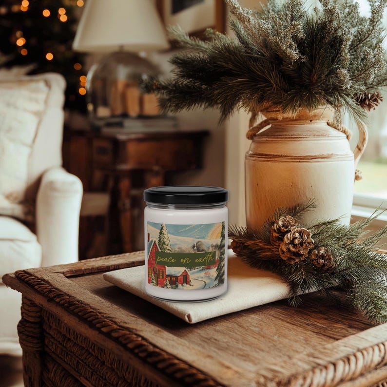 May include: A candle in a glass jar with a black lid. The label features a winter scene with a red house and the text "peace on earth" in gold. The candle sits on a wooden table.