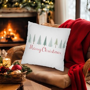 May include: White throw pillow with a row of green Christmas trees and the text "Merry Christmas" in red.