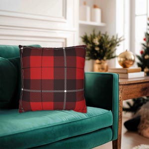 May include: A square throw pillow featuring a classic red and black plaid pattern with thin white intersecting lines. The fabric has a visible woven texture, and the pillow is displayed in a plump, filled shape with clean, straight edges.