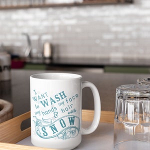 May include: White ceramic mug with a blue design that says "I want to wash my hands & hair with snow". The mug is on a wooden tray with a glass next to it.