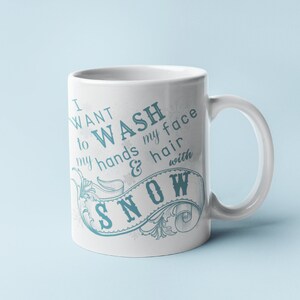 May include: White ceramic mug with a blue and white design. The mug features a decorative banner with the text "I want to wash my hands & hair with snow".