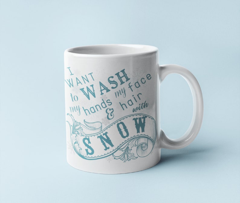 May include: White ceramic mug with a blue and white design. The mug features a decorative banner with the text "I want to wash my hands & hair with snow".