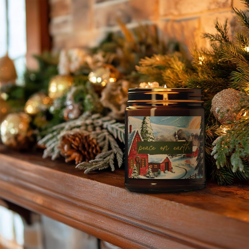 May include: A brown glass jar candle with a black lid, featuring a winter scene label with a red house and the text "peace on earth." The candle sits on a wooden surface, surrounded by Christmas decorations.